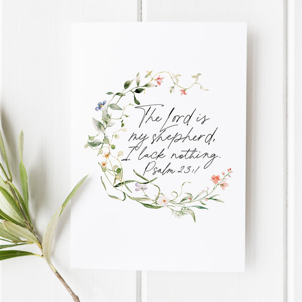 A Bible verse art print from Snow and Company featuring Psalm 23:1. The verse is written in a beautiful hand lettered font and is surrounded by a watercolor wildflower wreath. Cottage core. The perfect christian gift.
